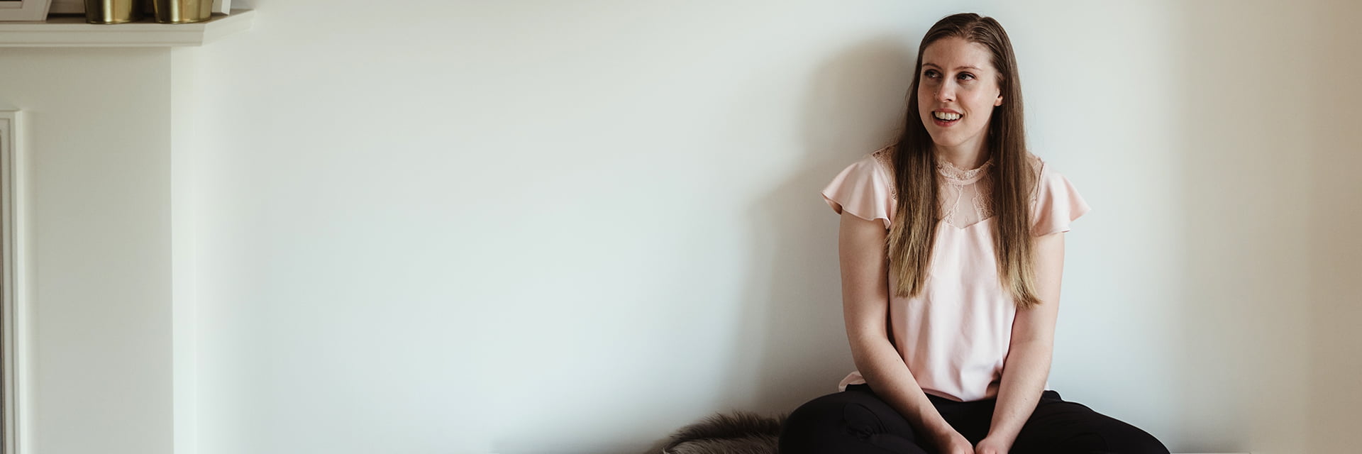 Hayley Moriarty sitting on bench against a wall in front of 4 framed pictures